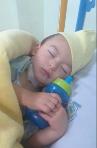 Mathi bebé dormido, envuelto en una toalla, con su biberón